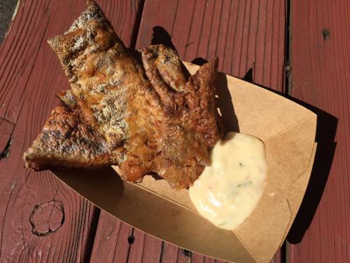 Crispy fried fish served on a paper tray with a side of creamy dipping sauce.