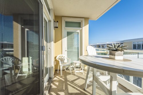 A sunny balcony with white chairs and a round table, featuring a small plant centerpiece and a clear blue sky.