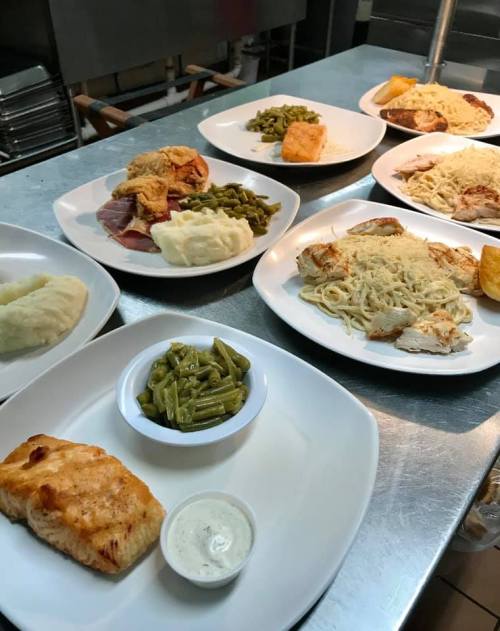 A variety of plated meals including chicken, salmon, green beans, mashed potatoes, and pasta on a kitchen counter.