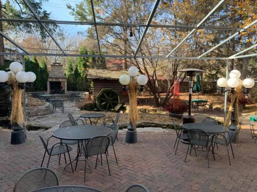 Outdoor patio with black tables, decorative white balloons, and a stone fireplace surrounded by trees in autumn.