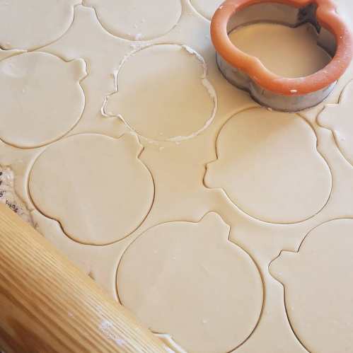 A rolling surface with circular cookie dough cutouts and a round cutter, ready for baking.