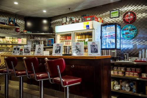 A retro diner counter with red stools, a fridge, and black-and-white photos of famous musicians on display.