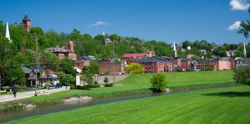 A scenic view of a small town with green hills, historic buildings, and a river under a clear blue sky.
