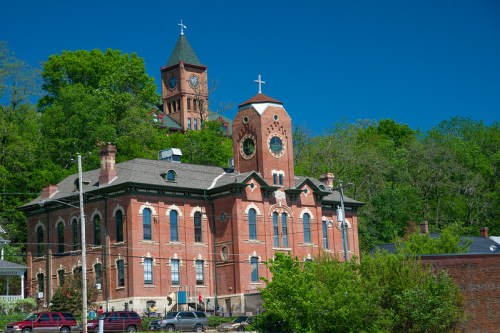 Historic brick building with a clock tower, surrounded by greenery and a clear blue sky.