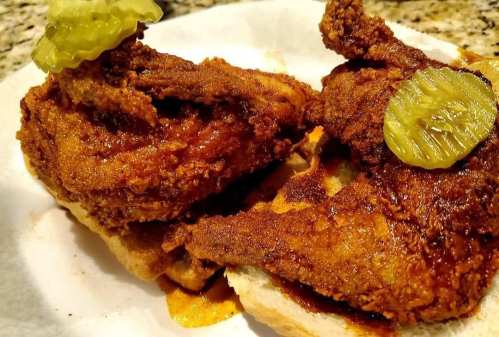 Two pieces of crispy fried chicken on bread, topped with pickles, served on a white paper plate.