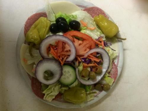 A colorful salad on a plate featuring lettuce, tomatoes, cucumbers, olives, peppers, and slices of salami and cheese.