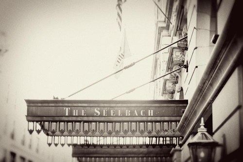 Black and white image of the Seelbach Hotel entrance sign with decorative lights and flags above.