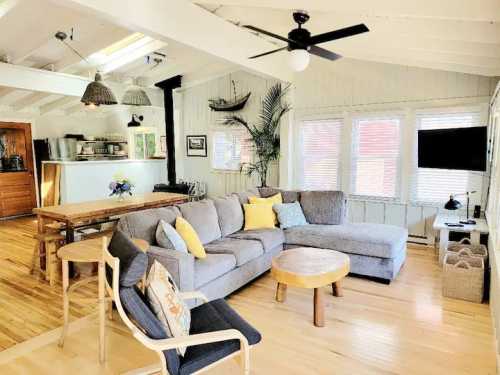 Cozy living room with a gray sectional sofa, wooden table, and bright windows, featuring a relaxed, inviting atmosphere.