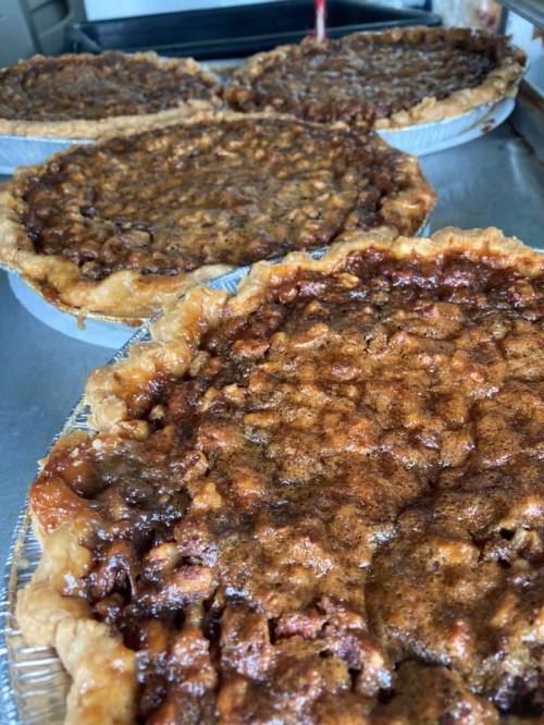 Four freshly baked pecan pies in aluminum pie tins, with golden-brown crusts and rich, glossy fillings.