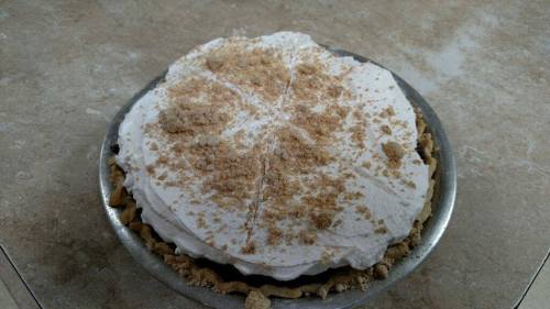A pie with a creamy topping and a crumbly texture, set in a metal pie dish on a light-colored countertop.