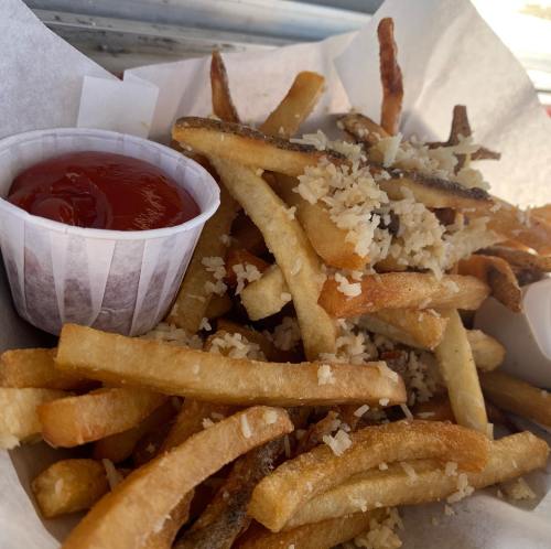A basket of crispy French fries topped with grated cheese and served with a side of ketchup.