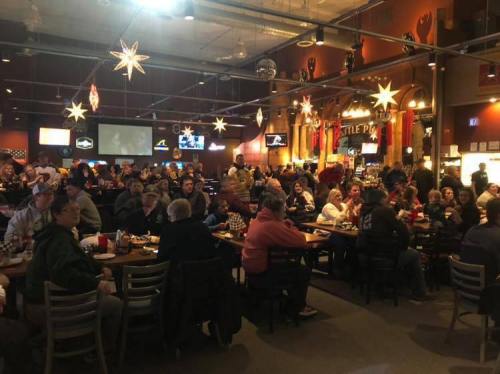 A crowded restaurant with people dining and socializing, decorated with stars and screens showing sports.