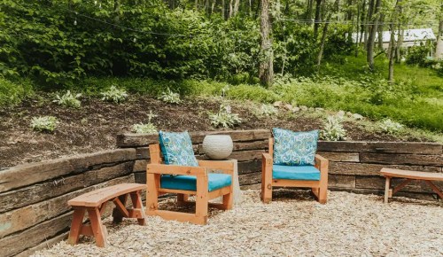 Cozy outdoor seating area with two blue cushioned chairs and a small table, surrounded by greenery and wood accents.