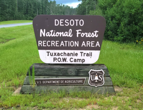 Sign for Desoto National Forest Recreation Area, featuring Tuxachanie Trail and P.O.W. Camp, with U.S. Department of Agriculture logo.