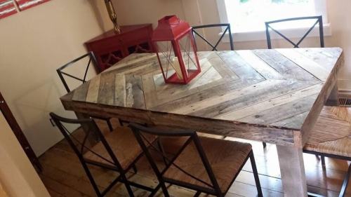 A wooden dining table with a chevron pattern, surrounded by black metal chairs and a red lantern on top.