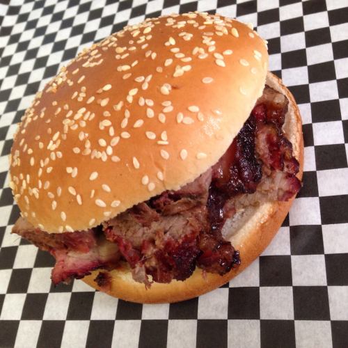 A sesame seed bun filled with smoky, sliced barbecue meat, resting on a black and white checkered paper.