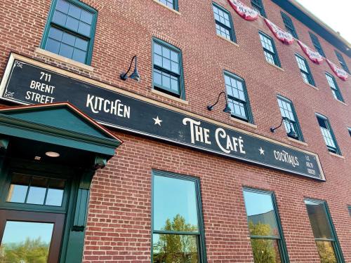 Sign for "The Café" with "Kitchen" and "Cocktails" on a brick building, featuring large windows and decorative elements.
