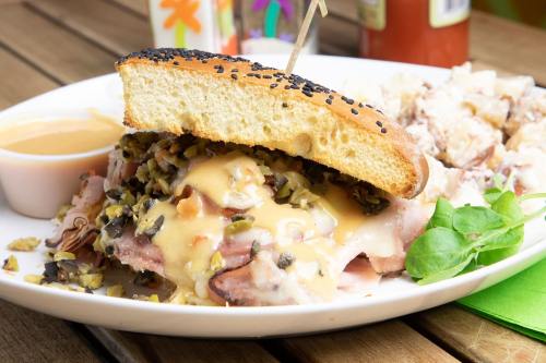 A close-up of a sandwich with ham, melted cheese, and pickles on a plate, accompanied by a side of salad and sauce.