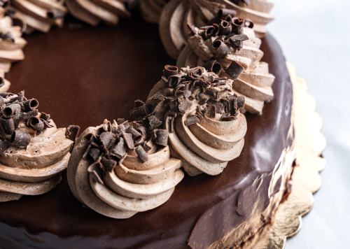 A close-up of a chocolate cake topped with swirls of chocolate frosting and chocolate shavings.