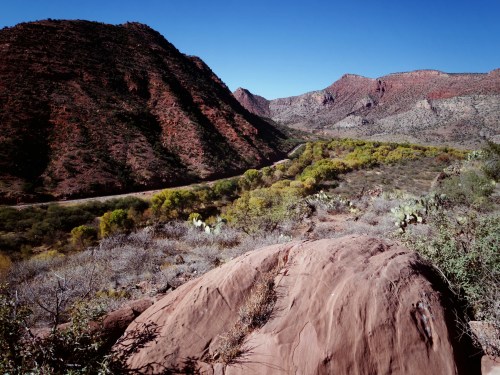 A scenic view of rugged mountains and a winding river, surrounded by green vegetation and rocky terrain under a clear blue sky.