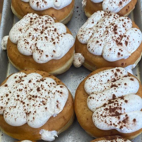 A tray of fluffy donuts topped with creamy white frosting and a dusting of cocoa powder.
