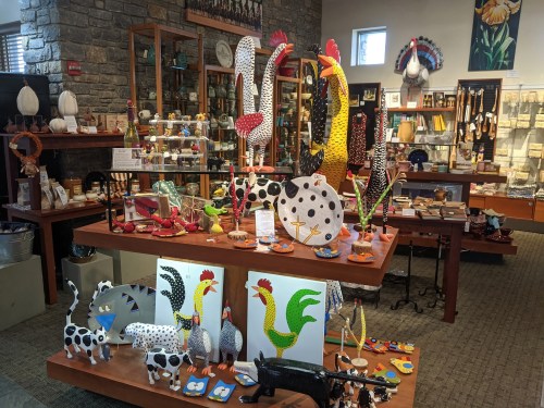 Colorful ceramic roosters and various handcrafted items displayed in a vibrant gift shop with stone walls.
