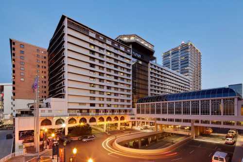 A modern urban hotel complex at dusk, featuring multiple buildings and a glass-covered walkway.