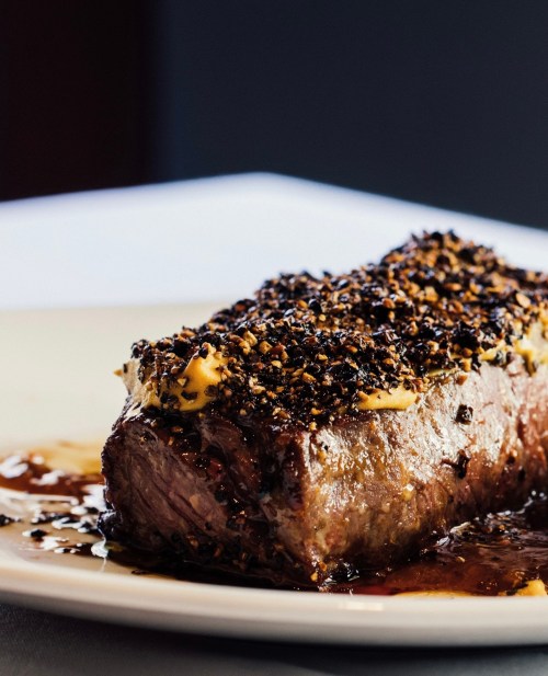A close-up of a juicy, seasoned beef roast with a dark crust and a rich sauce on a white plate.