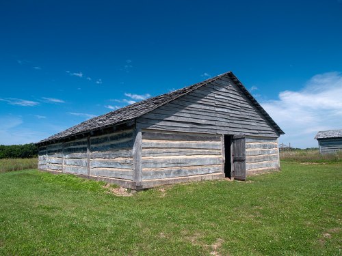 A rustic wooden building with a sloped roof, set against a clear blue sky and green grass.