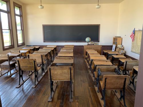 A vintage classroom with wooden desks, a chalkboard, a globe, and large windows, creating a nostalgic atmosphere.