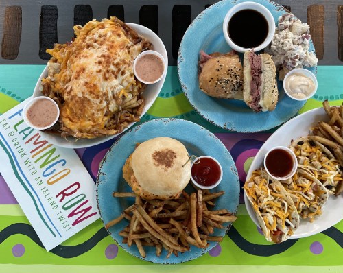 A colorful table spread featuring loaded fries, a sandwich, coleslaw, and a side of fries with dipping sauces.