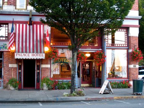 Historic Palace Hotel with red and white striped awning, surrounded by flowers and trees, in a charming street setting.