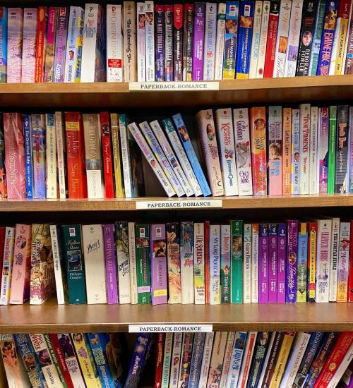 A bookshelf filled with various paperback romance novels, organized by title and author.