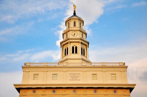 Clock tower with a golden statue on top, set against a blue sky with clouds. Building features ornate architectural details.