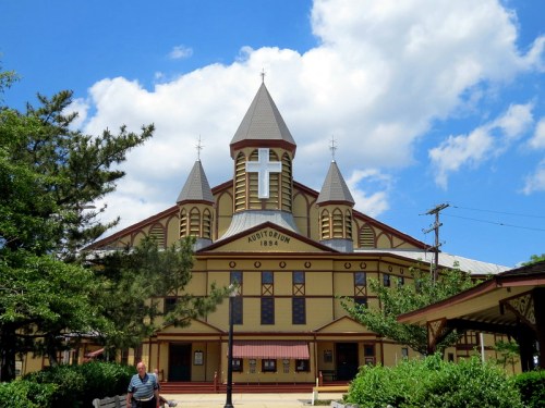 Historic auditorium with a cross on top, featuring three spires, surrounded by trees and a blue sky.