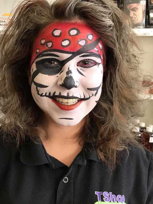 A person with pirate-themed face paint, featuring a skull design and a red bandana, smiling at the camera.