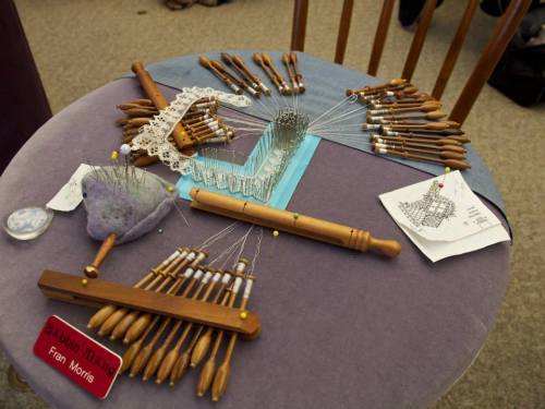 A table displaying lace-making tools, including bobbins, pins, and patterns, with a name tag reading "Fran Morris."