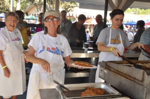 A group of people cooking and serving food at an outdoor event, with smiles and a festive atmosphere.
