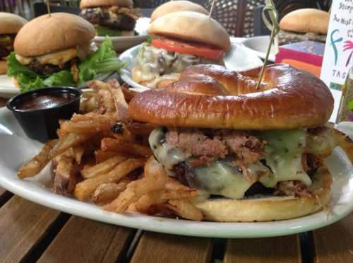 A close-up of a juicy burger with melted cheese and a side of crispy fries on a plate, with other burgers in the background.