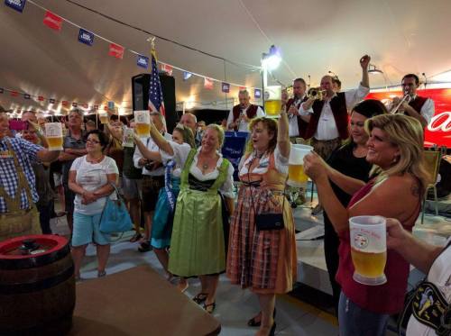 A lively festival scene with people in traditional attire raising beer mugs, celebrating with a band in the background.