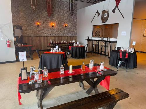 A spacious dining area with black tables, red accents, and rustic decor, featuring a stone wall and medieval-themed elements.