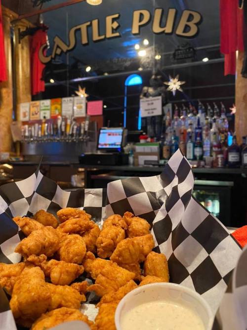 A basket of golden fried chicken bites with a side of dipping sauce, set against a pub backdrop.