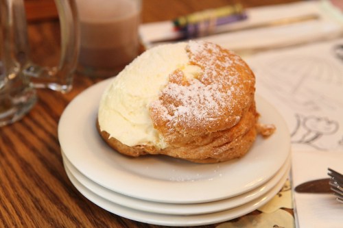 A fluffy pastry filled with cream, dusted with powdered sugar, on a stack of white plates.