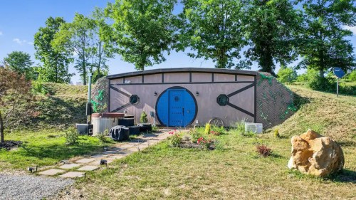 A unique, round building with a blue door, surrounded by greenery and a stone pathway.