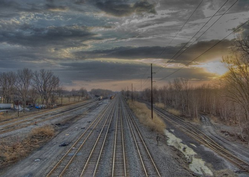 A desolate railway scene at sunset, with multiple tracks stretching into the distance under a cloudy sky.
