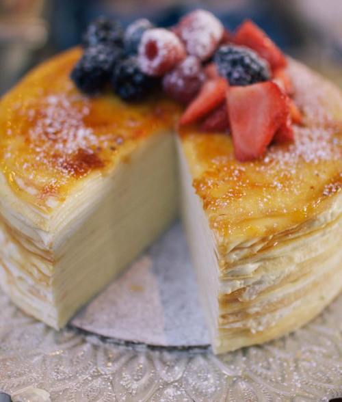 A layered cake with a slice cut out, topped with fresh berries and powdered sugar on a decorative plate.