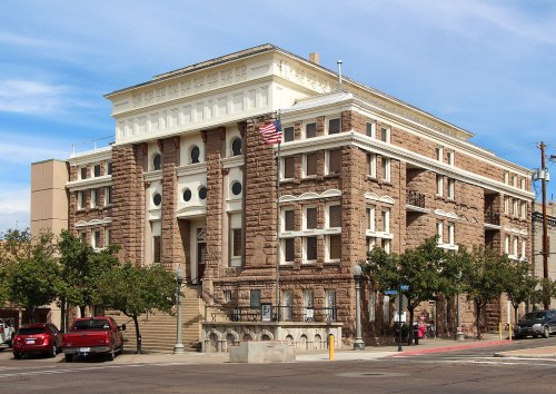 Historic stone building with ornate architecture, featuring large windows and an American flag, set against a blue sky.