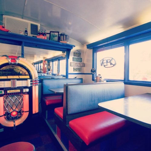 A retro diner interior featuring booths, a jukebox, and large windows with a cozy atmosphere.