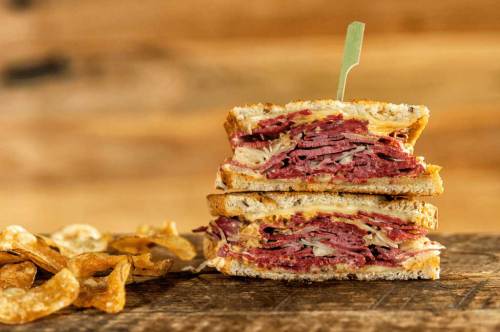 A stacked sandwich filled with layers of meat and cheese, served with crispy chips on a wooden surface.