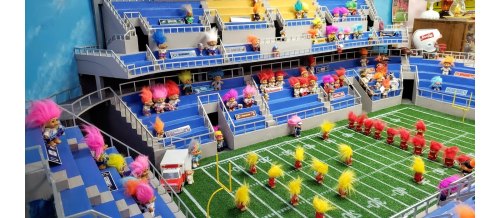A miniature football stadium filled with colorful troll dolls, some on the field and others in the stands.